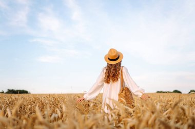 Şapkalı tatlı bir kadın gün batımında buğday tarlasında duruyor. Güzel bir kadın gün batımından zevk alır ve bir çiftlik arazisinde gezinir. Güzellik kavramı, doğa.