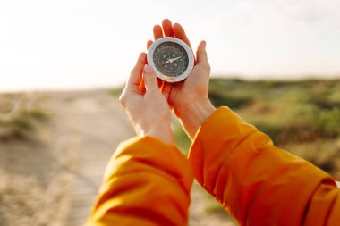 Deniz manzarasına karşı pusula tutan bir sırt çantasının yakın çekimi. Genç kadın güneşli bir günün tadını çıkarıyor ve yol tarifi arıyor. Navigasyon ve macera kavramları.
