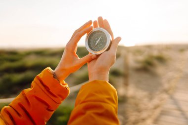 Deniz manzarasına karşı pusula tutan bir sırt çantasının yakın çekimi. Genç kadın güneşli bir günün tadını çıkarıyor ve yol tarifi arıyor. Navigasyon ve macera kavramları.