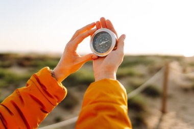 Deniz manzarasına karşı pusula tutan bir sırt çantasının yakın çekimi. Genç kadın güneşli bir günün tadını çıkarıyor ve yol tarifi arıyor. Navigasyon ve macera kavramları.