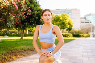Spor giyimli güzel bir kadın yeşil bir parkta ısınıyor. Açık havada egzersiz yapan atletik bir kadın. Spor, atletizm ve zevk kavramları.