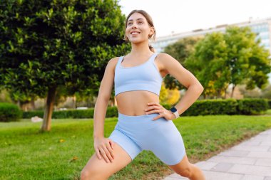 Spor giyimli güzel bir kadın yeşil bir parkta ısınıyor. Açık havada egzersiz yapan atletik bir kadın. Spor, atletizm ve zevk kavramları.