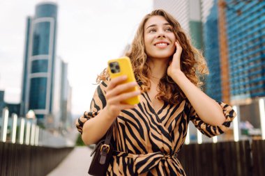 Elinde telefon olan genç bir kadın, şehir merkezine bakan yaya köprüsünde duruyor. Bir turist yürüyüş yapmaktan, mesajlaşmaktan ya da dışarıda blog yazmaktan hoşlanır. Günlük konsepti, yürüyüş.
