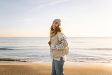 Güneşin doğuşunda güzel bir kadın sahilde duruyor. Bir gezgin eğleniyor, güneş ışınlarında su kenarında geziniyor. Seyahat, rahatlama ve yürüme kavramları.