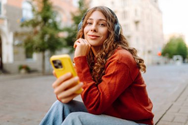 Kablosuz kulaklıkları ve telefonu olan neşeli bir kadın güneşli bir günde şehir ortamının tadını çıkarıyor. Genç bir kadın müzik dinler ve eski kasabada gezinir. Dinlenme ve rahatlama kavramı.