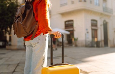 Güneşli bir sokakta parlak bir sırt çantasında bir turistin elinin yakın çekimi. Sırt çantalı genç bir kadın eski kasabada gezintiden hoşlanıyor. Seyahat ve eğlence kavramları.