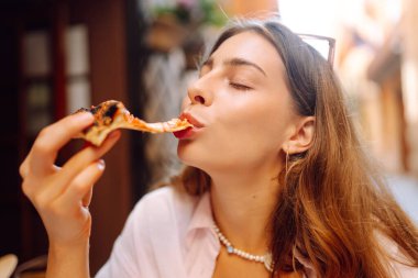 Restoran masasında güzel bir kadının portresi. Elinde bir dilim kokulu pizza var. Neşeli bir kadın gün batımında lezzetli bir İtalyan pizzasının tadını çıkarır. Konseptler: Gıda, turizm, keyif.