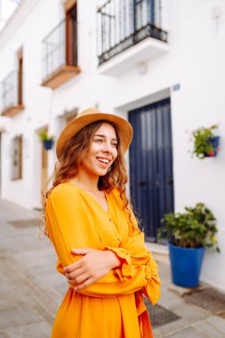 Sarı elbiseli ve şapkalı mutlu bir turist şehrin eski, güneşli caddelerinde geziniyor. Güzel bir kadın gün batımından zevk alır. Turizm kavramı, hafta sonu, dinlenme.