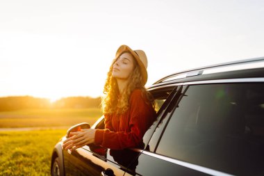 Şapkalı güzel bir kadın arabasının camından sarkarken kendini özgür hisseder. Genç bir kadın gün batımının tadını çıkarıyor ve bir yol gezisinde dinleniyor. Macera, ulaşım ve özgürlük kavramları.