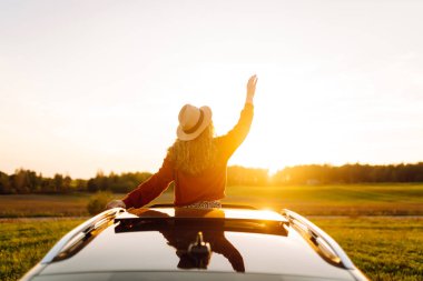 Şapkalı güzel bir kadın arabasının camından sarkarken kendini özgür hisseder. Genç bir kadın gün batımının tadını çıkarıyor ve bir yol gezisinde dinleniyor. Macera, ulaşım ve özgürlük kavramları.