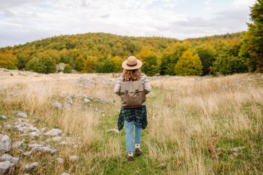 Arkadan bak. Sırt çantası ve şapkası olan bir yürüyüşçü kayalık dağ yolunda yürüyor. Genç kadın dağ manzarasının tadını çıkarıyor ve özgürlük duygusunu hissediyor. Yürüyüş, doğa ve seyahat kavramı.