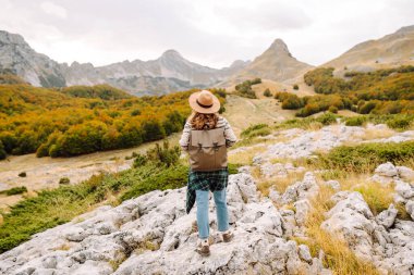 Arkadan bak. Sırt çantası ve şapkası olan bir yürüyüşçü kayalık dağ yolunda yürüyor. Genç kadın dağ manzarasının tadını çıkarıyor ve özgürlük duygusunu hissediyor. Yürüyüş, doğa ve seyahat kavramı.