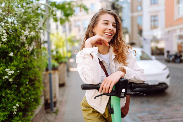 Neşeli bir kadın güneşli şehir caddelerinde elektrikli scooter kullanıyor. Genç bir turist modern bir scooterla gezmekten hoşlanıyor. Ekoloji ve yürüme kavramı.