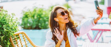 Şehirdeki bir bankta oturan ve telefonla konuşan bir kadın. Güneş gözlüklü bir turist elinde akıllı bir telefonla gülüyor. Güzellik anlayışı, moda. Kentsel yaşam tarzı.