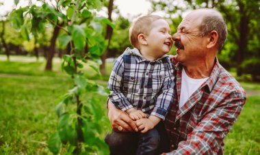 Bir büyükbaba ve torunu parkta otururken neşeyle burunlarına dokunurlar. Güneşli bir öğleden sonra yeşil çimenler ve ağaçlarla çevrilidir..