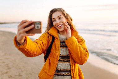 Sırt çantalı biri güneş ışınlarıyla sahilde selfie çeker. Genç bir kadın açık havada blog yazarak deniz kenarında vakit geçirmekten hoşlanıyor. Blog yazma, gevşeme ve hafta sonları için kavramlar.