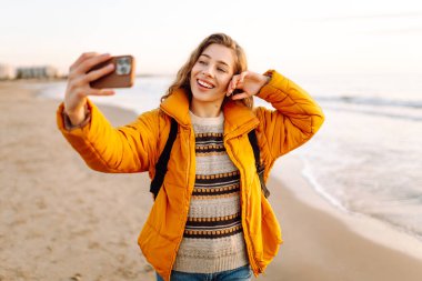 Sırt çantalı biri güneş ışınlarıyla sahilde selfie çeker. Genç bir kadın açık havada blog yazarak deniz kenarında vakit geçirmekten hoşlanıyor. Blog yazma, gevşeme ve hafta sonları için kavramlar.