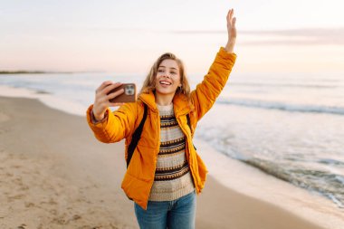 Sırt çantalı biri güneş ışınlarıyla sahilde selfie çeker. Genç bir kadın açık havada blog yazarak deniz kenarında vakit geçirmekten hoşlanıyor. Blog yazma, gevşeme ve hafta sonları için kavramlar.