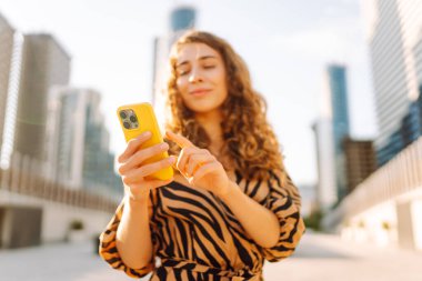 Metropol 'e tepeden bakan, akıllı telefona bakan bir kadının yakın çekimi. Kıvırcık saçlı güzel turist mesajlaşıyor ve yürüyüşten zevk alıyor. Konseptler: teknoloji, turizm, blog yazma.