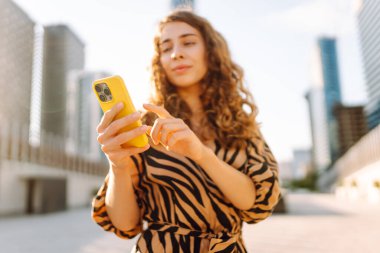 Metropol 'e tepeden bakan, akıllı telefona bakan bir kadının yakın çekimi. Kıvırcık saçlı güzel turist mesajlaşıyor ve yürüyüşten zevk alıyor. Konseptler: teknoloji, turizm, blog yazma.