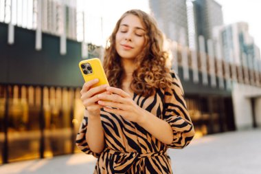 Metropol 'e tepeden bakan, akıllı telefona bakan bir kadının yakın çekimi. Kıvırcık saçlı güzel turist mesajlaşıyor ve yürüyüşten zevk alıyor. Konseptler: teknoloji, turizm, blog yazma.