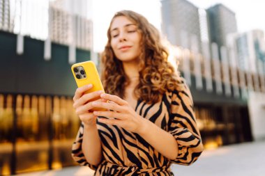 Metropol 'e tepeden bakan, akıllı telefona bakan bir kadının yakın çekimi. Kıvırcık saçlı güzel turist mesajlaşıyor ve yürüyüşten zevk alıyor. Konseptler: teknoloji, turizm, blog yazma.