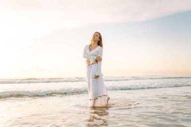 Genç bir kadın güneşli bir sahilde yürüyor, deniz manzarasının tadını çıkarıyor. Güzel bir kadın kendini özgür hisseder ve gün batımına hayran kalır. Kavram: rahatlama, doğa.