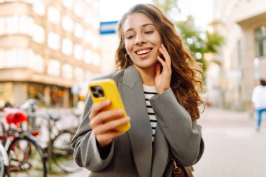 Güneşli bir günde şehir sokaklarında telefonu olan şık bir kadının portresi. Telefon mesajları atan ve gün batımında yürüyüş yapmaktan hoşlanan güzel bir kadın. Eğlence ve rahatlama kavramı.
