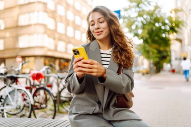 Güneşli bir günde şehir sokaklarında telefonu olan şık bir kadının portresi. Telefon mesajları atan ve gün batımında yürüyüş yapmaktan hoşlanan güzel bir kadın. Eğlence ve rahatlama kavramı.