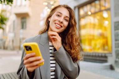 Güneşli bir günde şehir sokaklarında telefonu olan şık bir kadının portresi. Telefon mesajları atan ve gün batımında yürüyüş yapmaktan hoşlanan güzel bir kadın. Eğlence ve rahatlama kavramı.