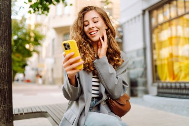 Güneşli bir günde şehir sokaklarında telefonu olan şık bir kadının portresi. Telefon mesajları atan ve gün batımında yürüyüş yapmaktan hoşlanan güzel bir kadın. Eğlence ve rahatlama kavramı.