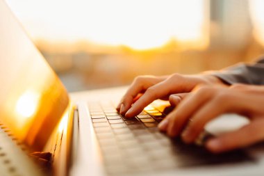 Günbatımında dizüstü bilgisayarda daktilo eden modern bir kadının yakın çekimi. Dişi bir serbest çalışan, dışarıda bir terasta dizüstü bilgisayarda çalışıyor. İş ve teknoloji kavramı.