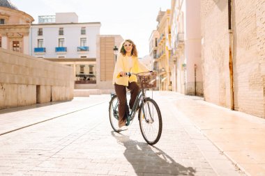 Neşeli bir kadın güneşli bir günde bisiklet sürmekten hoşlanır. Bir turist gün batımında bisiklet sürüyor, şehir sokaklarında geziniyor. Hafta sonu konsepti, turizm.
