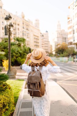 Şapkalı ve sırt çantalı güzel bir turist şehrin güneşli sokaklarında geziniyor. Mutlu bir kadın günbatımında Central Square 'in mimarisine hayran. Turizm kavramları, yürüyüş. Seyahat tutkusu.