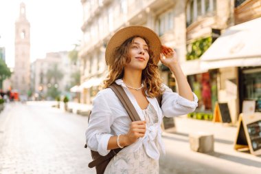 Şapkalı ve sırt çantalı güzel bir turist şehrin güneşli sokaklarında geziniyor. Mutlu bir kadın günbatımında Central Square 'in mimarisine hayran. Turizm kavramları, yürüyüş. Seyahat tutkusu.