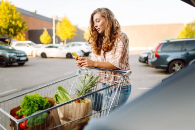 Park yerinde arabasının yanında taze yiyeceklerle duran genç bir kadının portresi. Güzel bir kadın arabanın bagajına meyve ve sebze koyar. Alışveriş, tüketim ve kentsel yaşam kavramları.