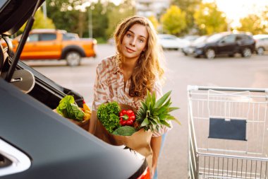 Park yerinde arabasının yanında taze yiyeceklerle duran genç bir kadının portresi. Güzel bir kadın arabanın bagajına meyve ve sebze koyar. Alışveriş, tüketim ve kentsel yaşam kavramları.