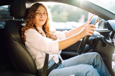 Kıvırcık saçlı genç bir kadın güneşin altında bir arabanın direksiyonunda oturur. Bir kadın sürücü güneşli bir günün tadını çıkarır. Taksi şöförü. Ulaşım kavramı, boş zaman.