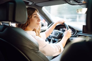 Kıvırcık saçlı genç bir kadın güneşin altında bir arabanın direksiyonunda oturur. Bir kadın sürücü güneşli bir günün tadını çıkarır. Taksi şöförü. Ulaşım kavramı, boş zaman.