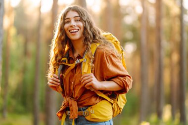 Güneşli bir ormanda yürüyüş parkurunda yürüyüş yapan sırt çantalı genç bir kadının portresi. Gezgin doğayı ve macerayı sever. Seyahat ve doğa kavramı, yürüyüş..