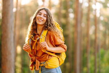 Güneşli bir ormanda yürüyüş parkurunda yürüyüş yapan sırt çantalı genç bir kadının portresi. Gezgin doğayı ve macerayı sever. Seyahat ve doğa kavramı, yürüyüş..