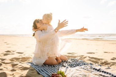 Mutlu anne ve küçük kızı sahilde birlikte eğleniyor, güneşte sarılıyorlar. Genç bir kadın ve küçük bir kız sahilde birlikte vakit geçiriyorlar. Çocukluk kavramları, annelik, rahatlama..