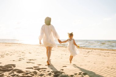 Mutlu anne ve küçük kızı sahilde birlikte eğleniyor, güneşte sarılıyorlar. Genç bir kadın ve küçük bir kız sahilde birlikte vakit geçiriyorlar. Çocukluk kavramları, annelik, rahatlama..