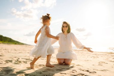 Mutlu anne ve küçük kızı sahilde birlikte eğleniyor, güneşte sarılıyorlar. Genç bir kadın ve küçük bir kız sahilde birlikte vakit geçiriyorlar. Çocukluk kavramları, annelik, rahatlama..