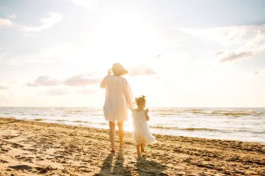 Mutlu anne ve küçük kızı sahilde birlikte eğleniyor, güneşte sarılıyorlar. Genç bir kadın ve küçük bir kız sahilde birlikte vakit geçiriyorlar. Çocukluk kavramları, annelik, rahatlama..