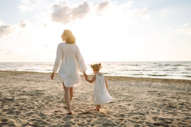 Mutlu anne ve küçük kızı sahilde birlikte eğleniyor, güneşte sarılıyorlar. Genç bir kadın ve küçük bir kız sahilde birlikte vakit geçiriyorlar. Çocukluk kavramları, annelik, rahatlama..