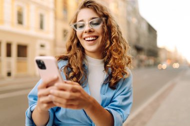 Güneşli bir caddede telefonuyla konuşan bir kadının portresi. Telefonu olan şık bir kadın dışarıda yürüyor. Blog yazma, yürüme ve turizm kavramları.