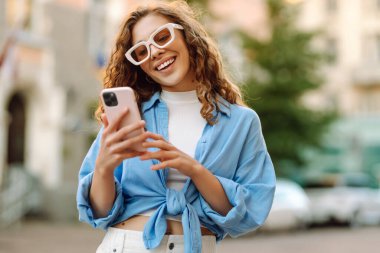 Güneşli bir caddede telefonuyla konuşan bir kadının portresi. Telefonu olan şık bir kadın dışarıda yürüyor. Blog yazma, yürüme ve turizm kavramları.