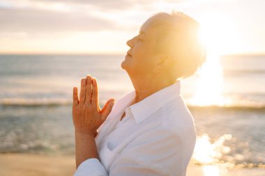 Gün batımında deniz kıyısında beyaz saçlı bir kadının portresi, deniz manzarasının tadını çıkarıyor. Yaşlı bir kadın sahilde kendini özgür hisseder. Mutlu emeklilik, rahatlama ve meditasyon kavramı.