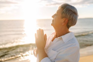 Gün batımında deniz kıyısında beyaz saçlı bir kadının portresi, deniz manzarasının tadını çıkarıyor. Yaşlı bir kadın sahilde kendini özgür hisseder. Mutlu emeklilik, rahatlama ve meditasyon kavramı.